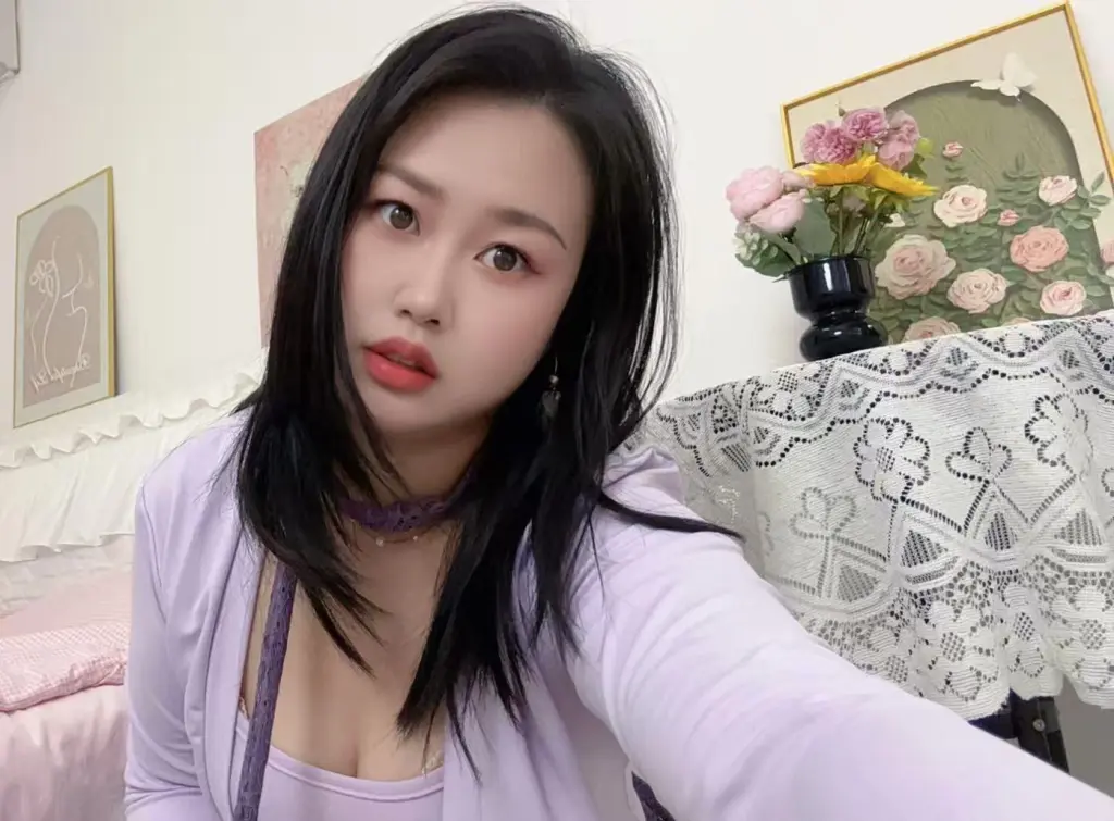 Lrenelvy poses close-up with long black hair, wearing a light yellow top in an indoor setting.