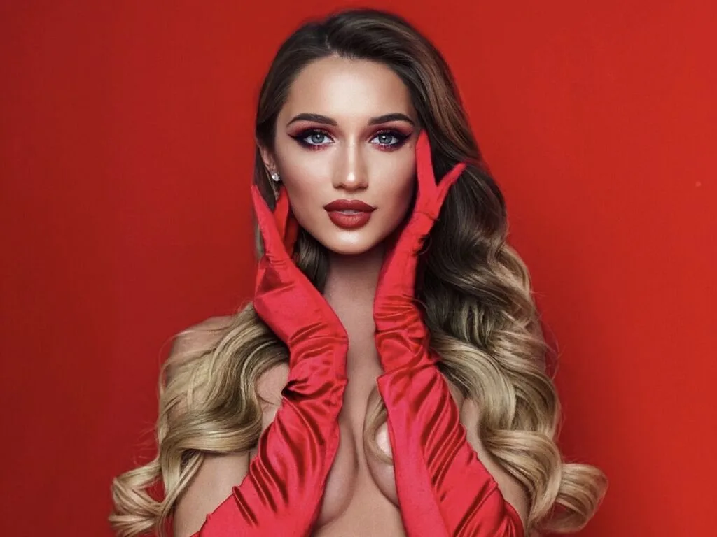 JanePortmans poses against a red background wearing long red satin gloves and red lipstick.