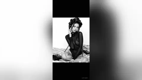 Glamorous woman in a black bodysuit with vintage hair rollers using a retro rotary telephone in black and white.