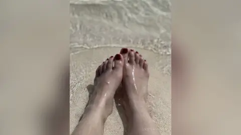 Close-up of bare feet resting in shallow ocean waves on a sandy beach during a relaxing summer day.