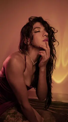Dreamy portrait of a woman in a burgundy silk dress with wavy hair in warm, moody lighting.