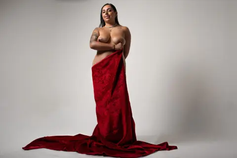 Confident woman wrapped in a luxurious red velvet fabric against a minimalist white studio background.