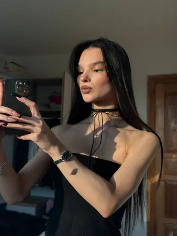 Noirbeauty poses for a mirror selfie wearing a black tube top and a thin black choker, showing off her long dark hair.