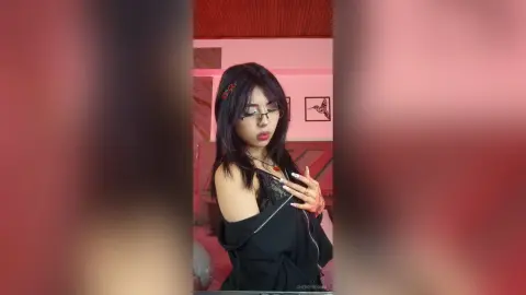 Young woman with dark hair in a black lace top posing in a pink bedroom with a moody aesthetic.