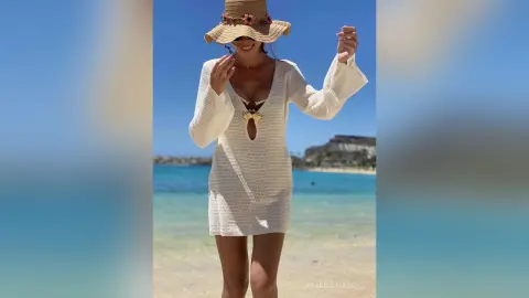 Cheerful woman in a white crochet mini dress and straw sun hat relaxing on a sunny tropical beach.