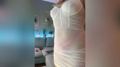 Woman in a white sheer corset dress posing in a modern living room with a soft, airy mood.