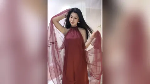 KireliaYan — KireliaYan poses in a long red halter dress while holding up a sheer red fabric veil.