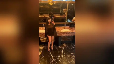 JuliDeming posing in a black mini dress and heels for a mirror selfie in a luxury bathroom.