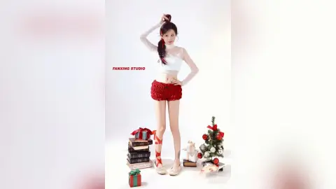 Young woman in white long-sleeve top and red shorts posing by a small Christmas tree and gift boxes.