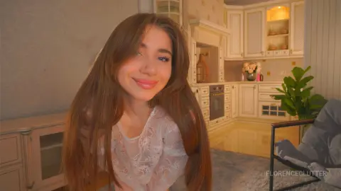Smiling young woman in a white lace blouse relaxing in a warm, cozy modern kitchen setting.