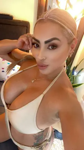 Glamorous blonde woman in a cream bikini and pearl headband posing indoors with a confident mood.