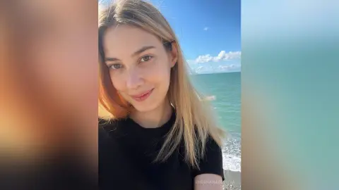 Smiling blonde woman in a black t-shirt enjoying a sunny day at the beach.