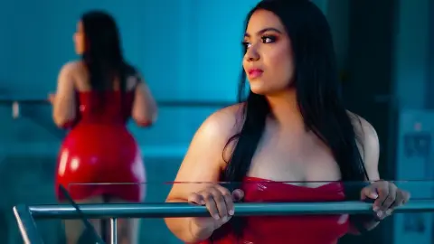 Elegant woman in a red strapless dress posing by a glass railing in a modern blue-toned setting.