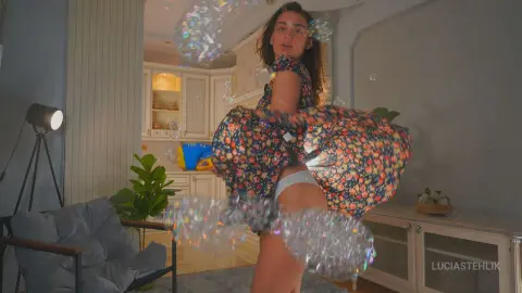 Young woman in a floral dress playing with bubbles in a bright, cozy living room.