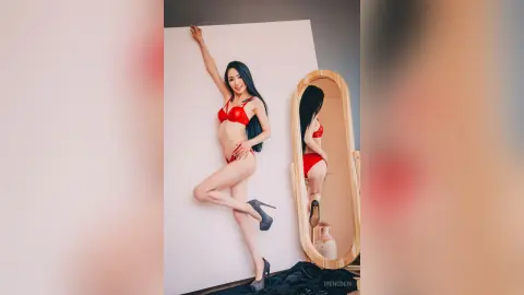 Smiling woman in a red bikini posing confidently in a minimalist studio setting.