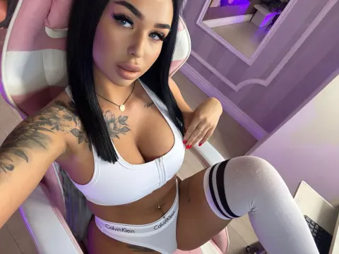 Tattooed woman in white sports bra and Calvin Klein underwear relaxing in a pink gaming chair.