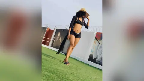 Stylish woman in black crop top and shorts posing on a rooftop garden under a clear sky.