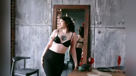 Confident woman in black bra and trousers posing in a moody, industrial loft setting.