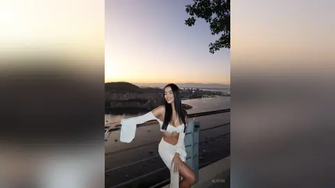 Alison poses on a balcony at sunset wearing a white off-the-shoulder crop top and matching skirt.