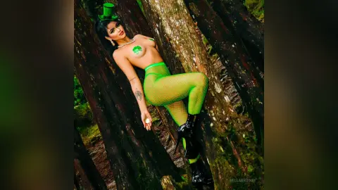 Woman in green fishnet tights and top posing against forest trees in a playful outdoor setting.