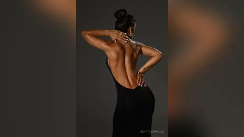 Elegant woman in a backless black evening gown posing against a dark studio background.