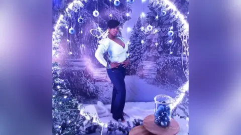 Smiling woman in a white blouse and blue jeans posing in a magical winter wonderland with blue holiday lights.