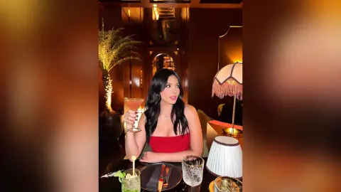 Elegant woman in a red top enjoying a cocktail in a moody, dimly lit upscale lounge setting.