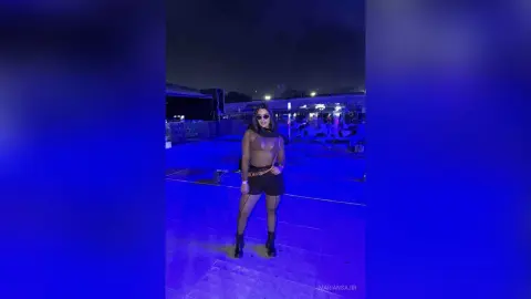 Stylish woman in black crop top and shorts posing under blue neon lights at a night rooftop party.