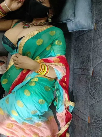 Woman in a teal and pink polka dot saree with gold jewelry relaxing on a blue textured sofa.