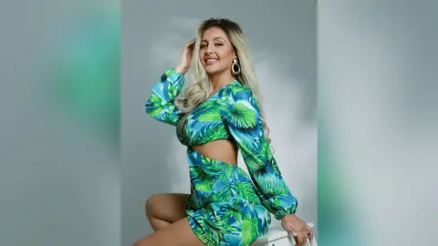 Anita smiles while wearing a long-sleeved, cut-out green tropical leaf print bodysuit against a grey background.