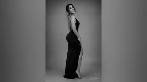 Elegant woman in a black backless evening gown posing in a moody black and white studio portrait.
