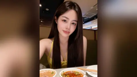 Young woman in a yellow tank top smiling at a restaurant table with bowls of ramen.
