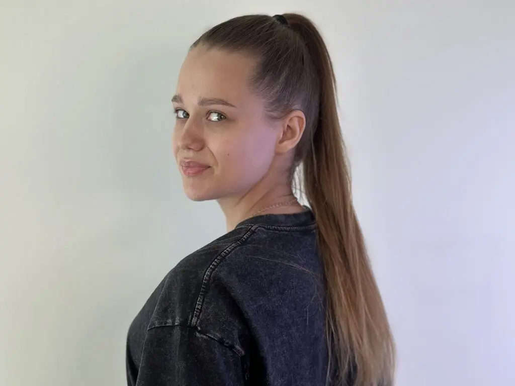 Smiling young woman with a high ponytail wearing a casual black sweatshirt against a plain white background.
