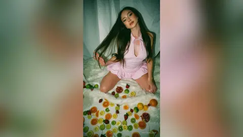 Young woman in a pink halter dress sitting on a white faux fur rug surrounded by colorful sliced citrus fruits.