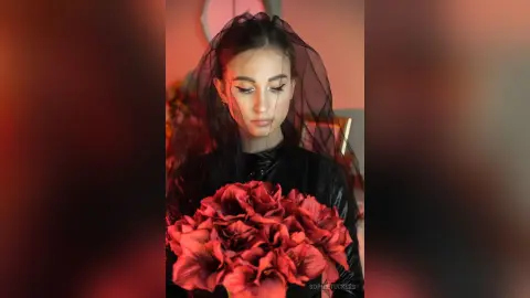 Moody portrait of a woman in a black outfit holding a large red rose bouquet in a dimly lit room.