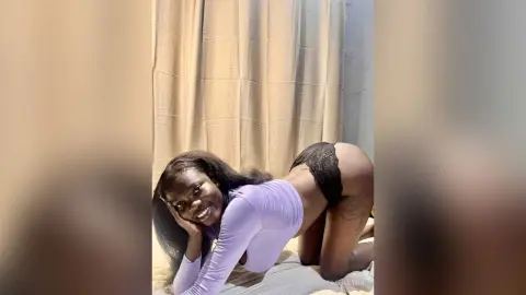 TashaLynn — TashaLynn smiles while kneeling on a bed, wearing a long-sleeved purple top and black lace panties that show her bare buttocks.
