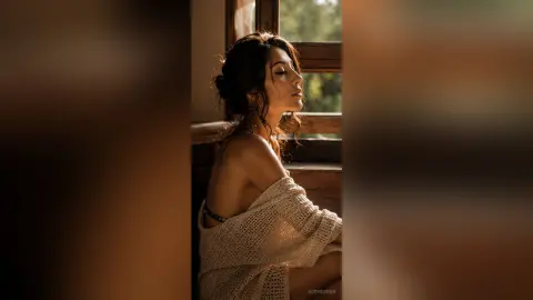 LorineSwan poses in profile wearing a white knit sweater that slips off her shoulder, showing her bare back and neck in warm lighting.