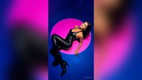 Stylish woman in a black bodysuit posing against a vibrant pink and blue neon circular background.