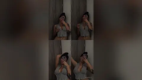 Young woman in a grey sleeveless top taking a moody mirror selfie in a dimly lit room.