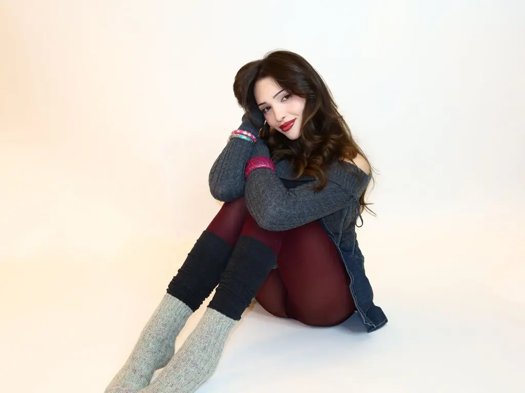 Brunette woman in a grey sweater and burgundy leggings sitting on a white background with a relaxed mood.