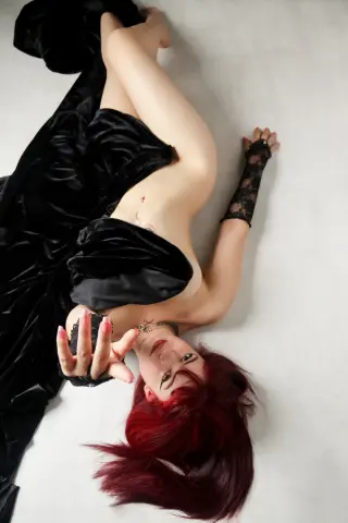 Elegant woman with red hair in a black velvet gown lying on a white floor for a moody, glamorous portrait.