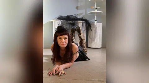 SabrinaBauer — SabrinaBauer lies on the floor wearing a black top and leopard print leggings with a black mesh fabric behind her.