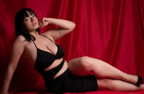 Elegant woman in a black cocktail dress posing against a red velvet curtain backdrop.