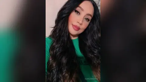 Smiling woman with long wavy dark hair wearing a green shirt in a bright indoor setting.