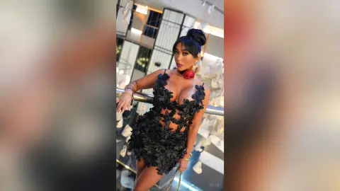 Dolce poses in a black floral lace mini dress with a plunging neckline, showing off her cleavage and dark hair styled in a high bun.