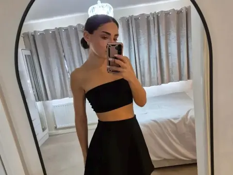 Young woman in a black strapless crop top and skirt taking a mirror selfie in a bright bedroom.