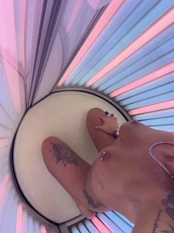 Tattooed woman sitting in a modern pink and blue neon light booth for a moody aesthetic portrait.