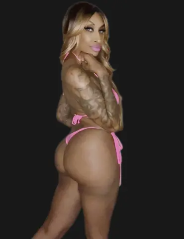 Tattooed woman in a pink string bikini posing confidently against a black background.