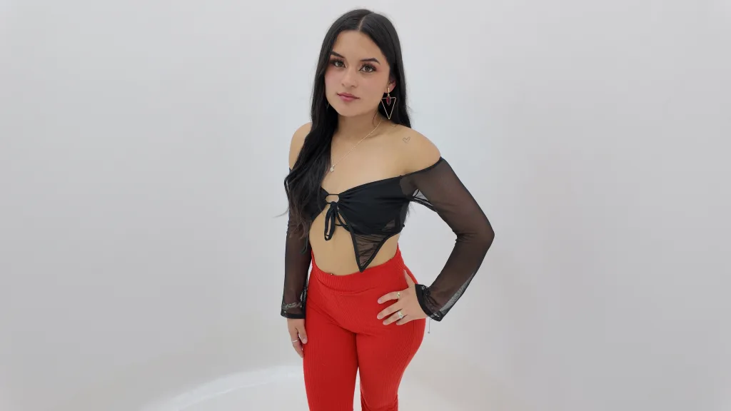 Valery_Rousse poses with long dark hair and a black sheer mesh top against a plain white background.