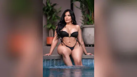 DayanaHille poses in a black bikini while sitting on the edge of a swimming pool.